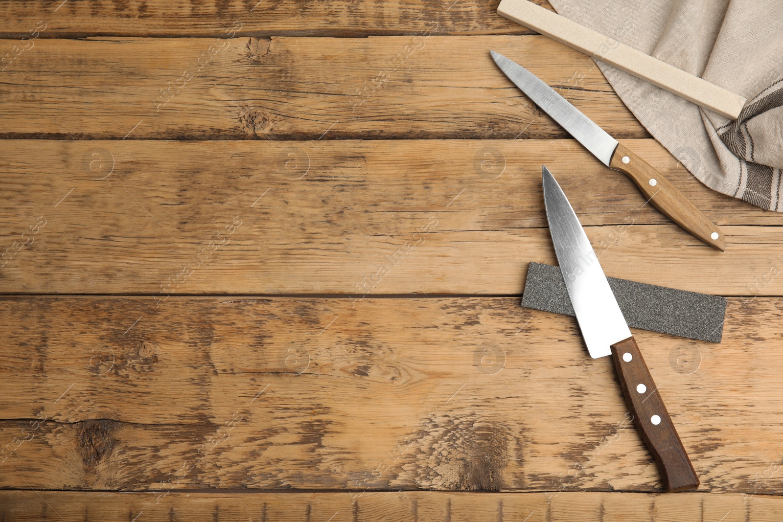 Photo of Sharpening stones and knives on wooden table, flat lay. Space for text