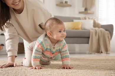 Photo of Happy young mother watching her cute baby crawl on floor at home