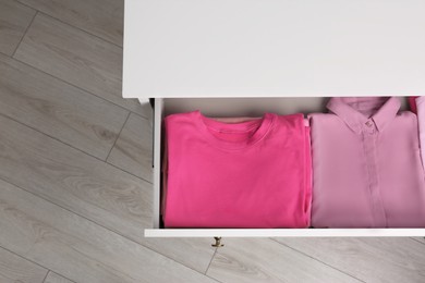 Photo of Folded pink clothes in white chest of drawers indoors, top view. Space for text