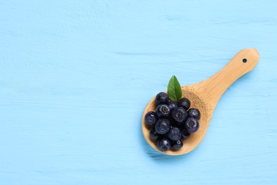 Spoon with ripe bilberries and leaf on light blue wooden table, top view. Space for text