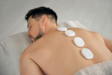 Photo of Handsome man receiving hot stone massage in spa salon