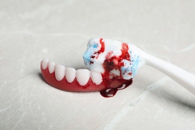 Photo of Gum model and toothbrush with blood on light grey table, closeup