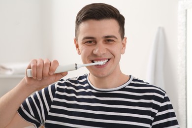 Photo of Man brushing his teeth with electric toothbrush in bathroom