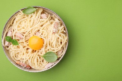 Photo of Bowl of tasty pasta Carbonara with basil leaves on light green background, top view. Space for text