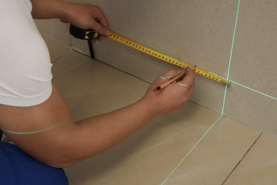 Photo of Worker using cross line laser level, pencil and tape for accurate measurement on plasterboard, closeup