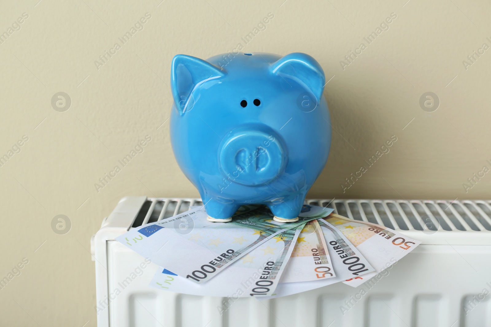 Photo of Piggy bank and euro banknotes on heating radiator against beige background