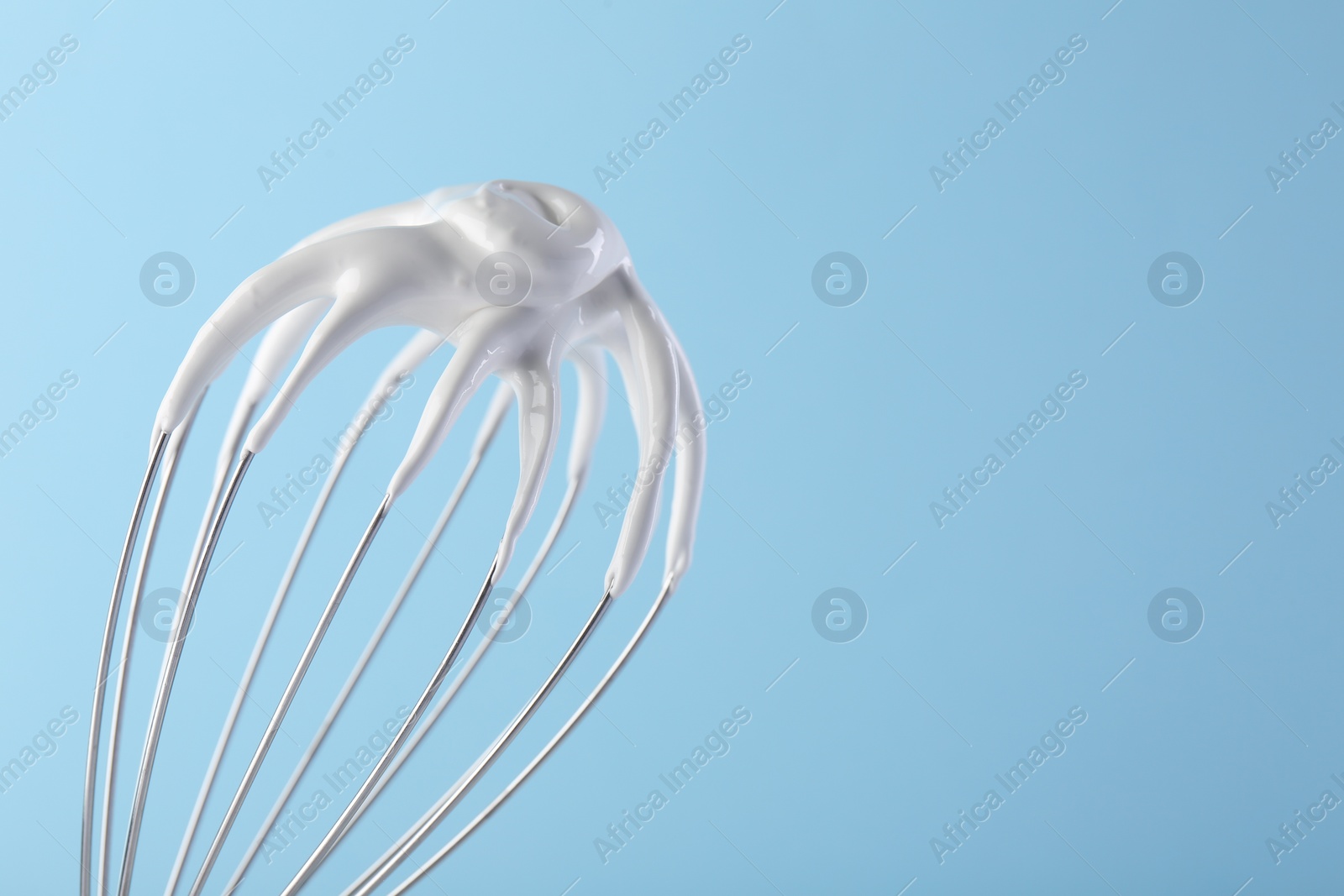 Photo of Whisk with whipped cream on light blue background, closeup. Space for text