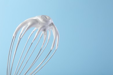 Whisk with whipped cream on light blue background, closeup. Space for text