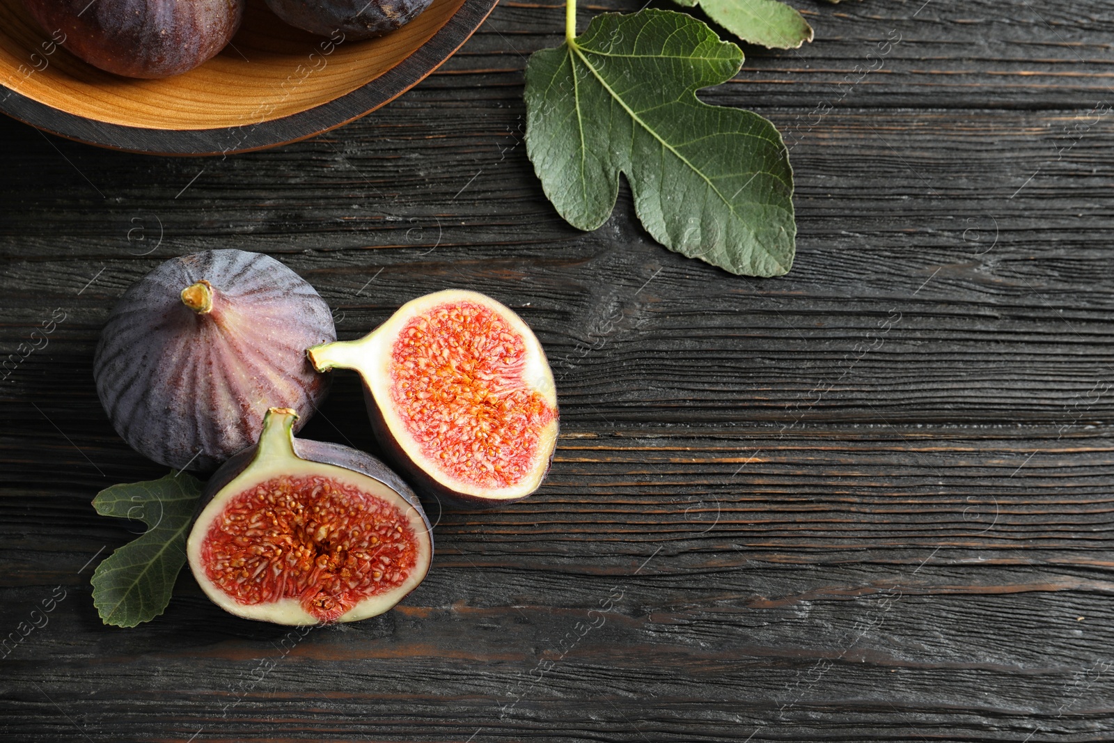 Photo of Fresh ripe figs with leaves on wooden table, top view. Space for text