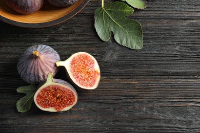 Photo of Fresh ripe figs with leaves on wooden table, top view. Space for text