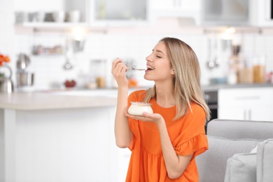 Photo of Young attractive woman eating tasty yogurt in kitchen