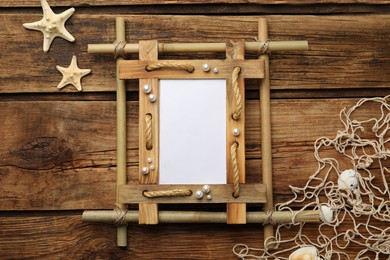 Photo of Empty bamboo frame, starfishes, seashells and fishing net on wooden table, flat lay