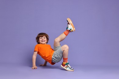 Photo of Happy little boy dancing on violet background. Space for text