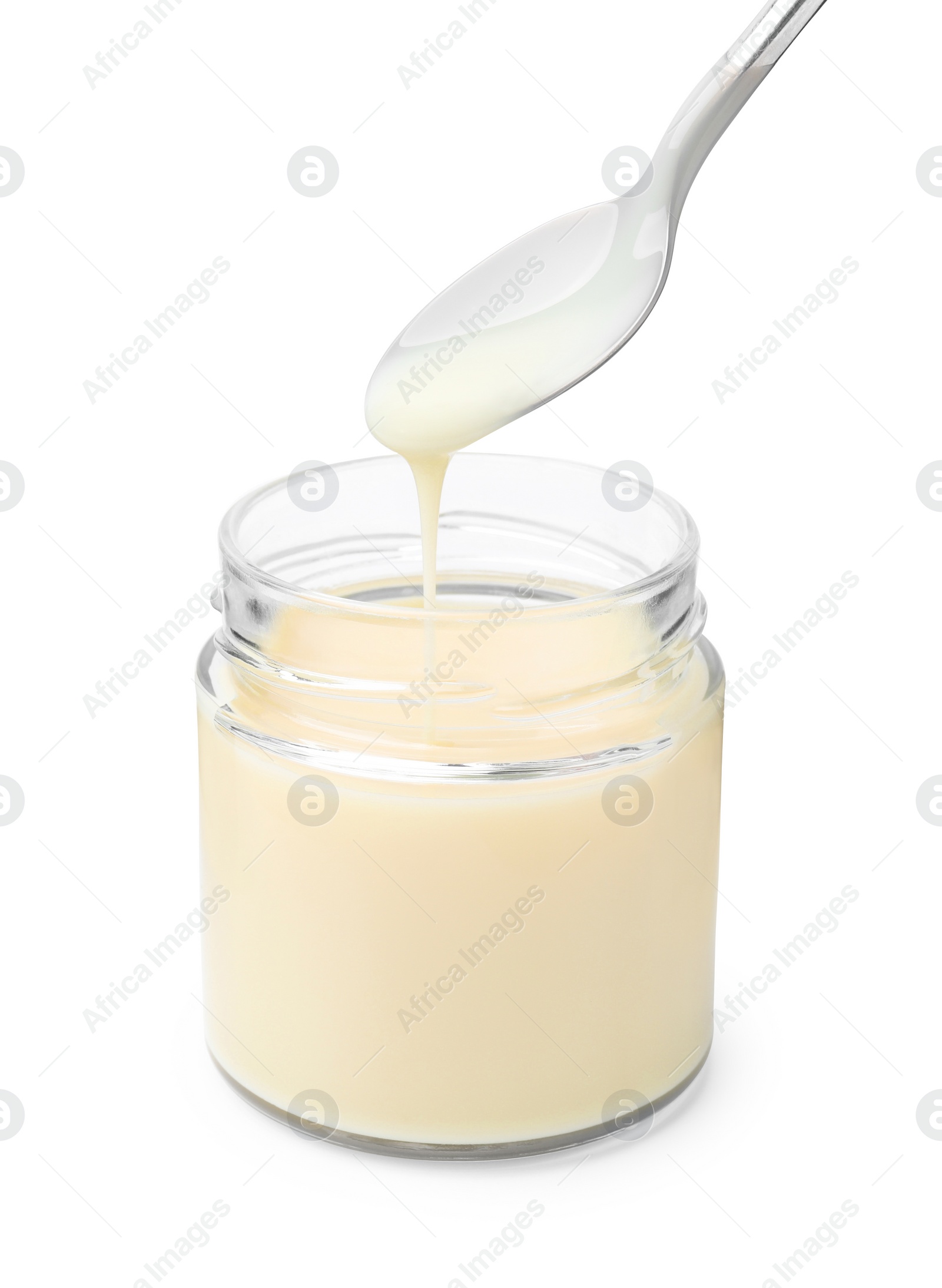 Photo of Condensed milk flowing down from spoon into jar isolated on white