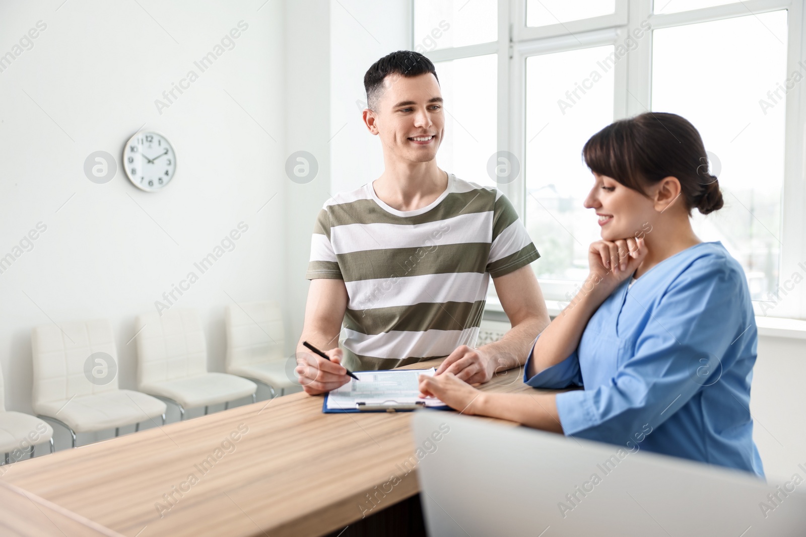 Photo of Smiling medical assistant working with patient at hospital reception. Space for text