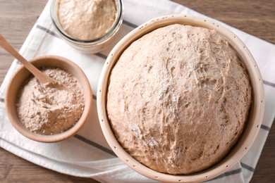 Photo of Fresh sourdough in proofing basket and flour on wooden table, top view