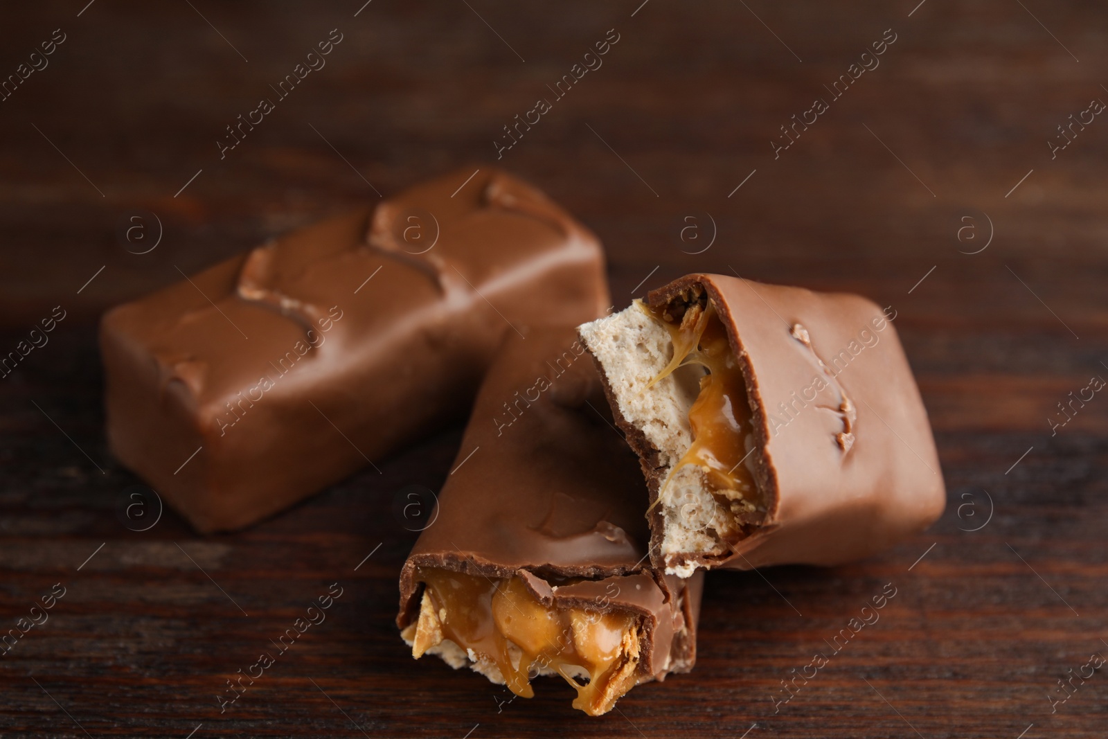 Photo of Chocolate bars with caramel, nuts and nougat on wooden table, closeup