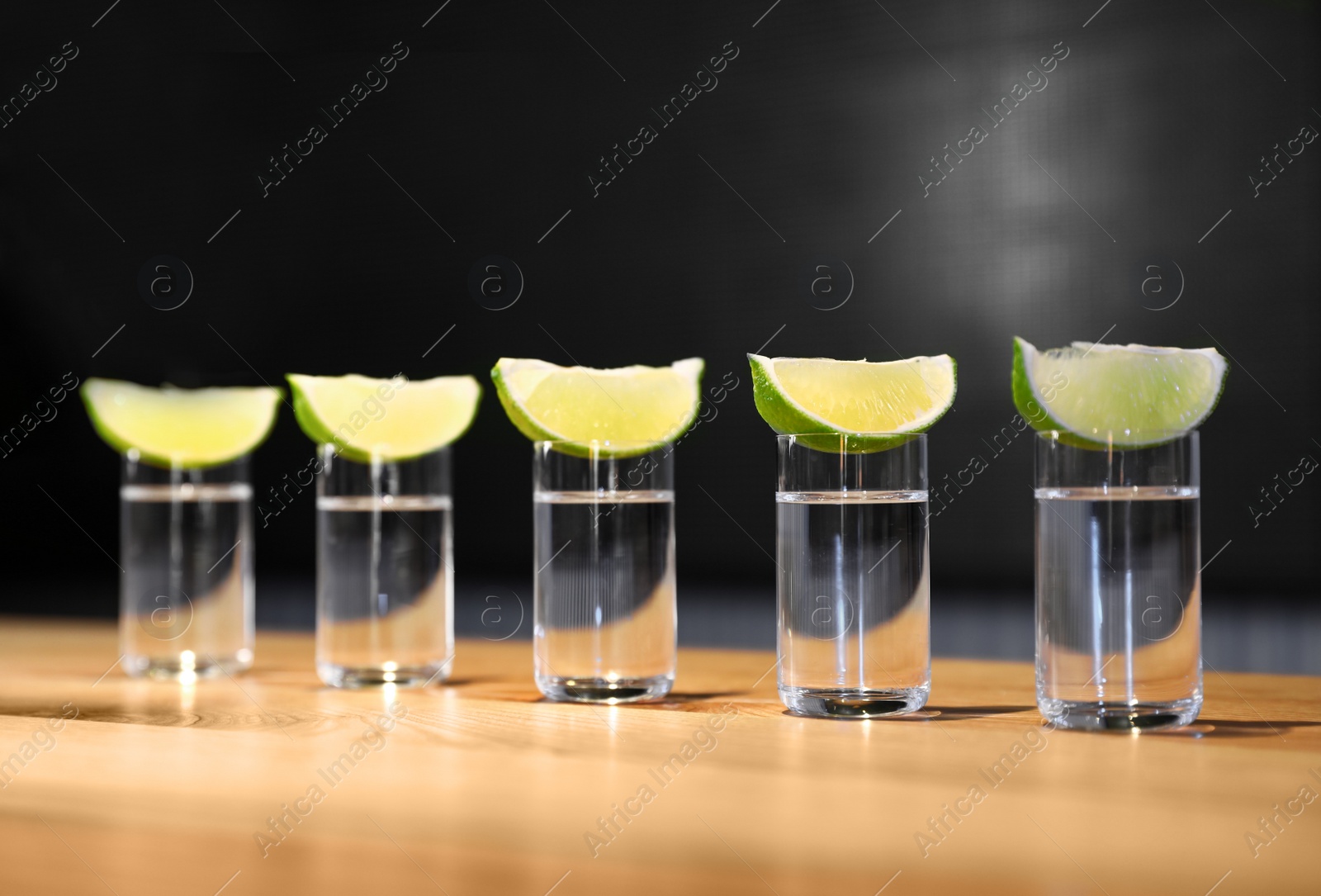 Photo of Vodka shots and lime slices on wooden bar counter