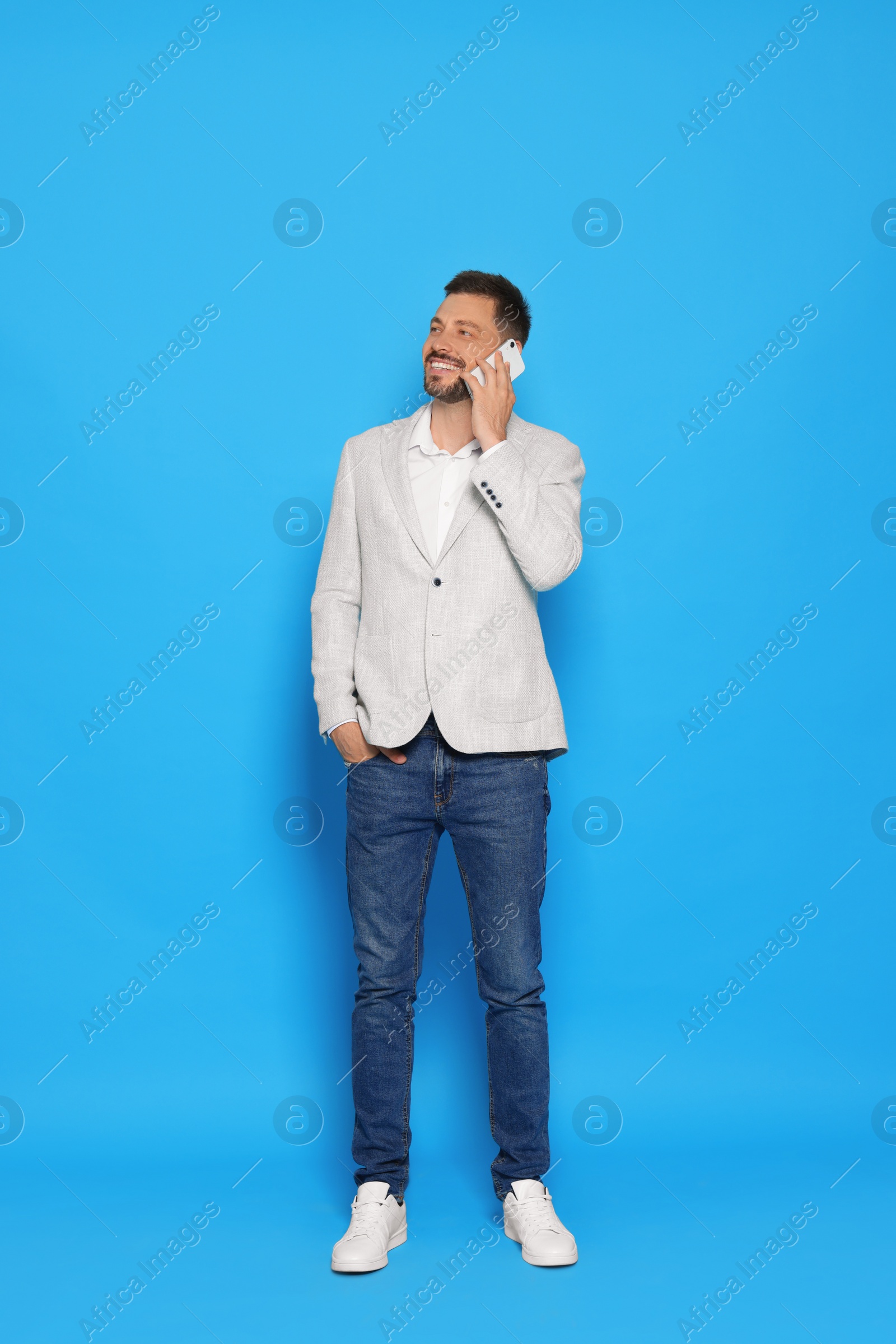 Photo of Handsome man talking on phone against light blue background