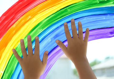 Child touching picture of rainbow on window, closeup. Stay at home concept