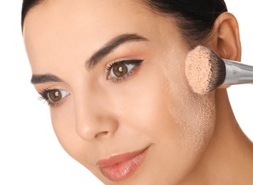 Beautiful young woman applying face powder with brush on white background, closeup