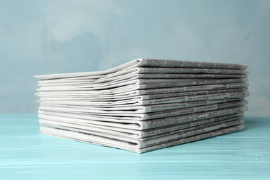 Photo of Stack of newspapers on light blue wooden table. Journalist's work
