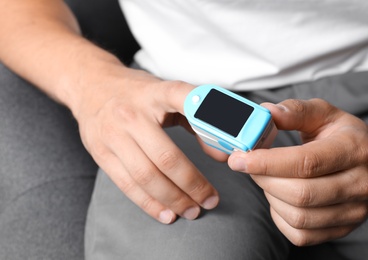 Photo of Young man checking pulse with blood pressure monitor on finger, closeup