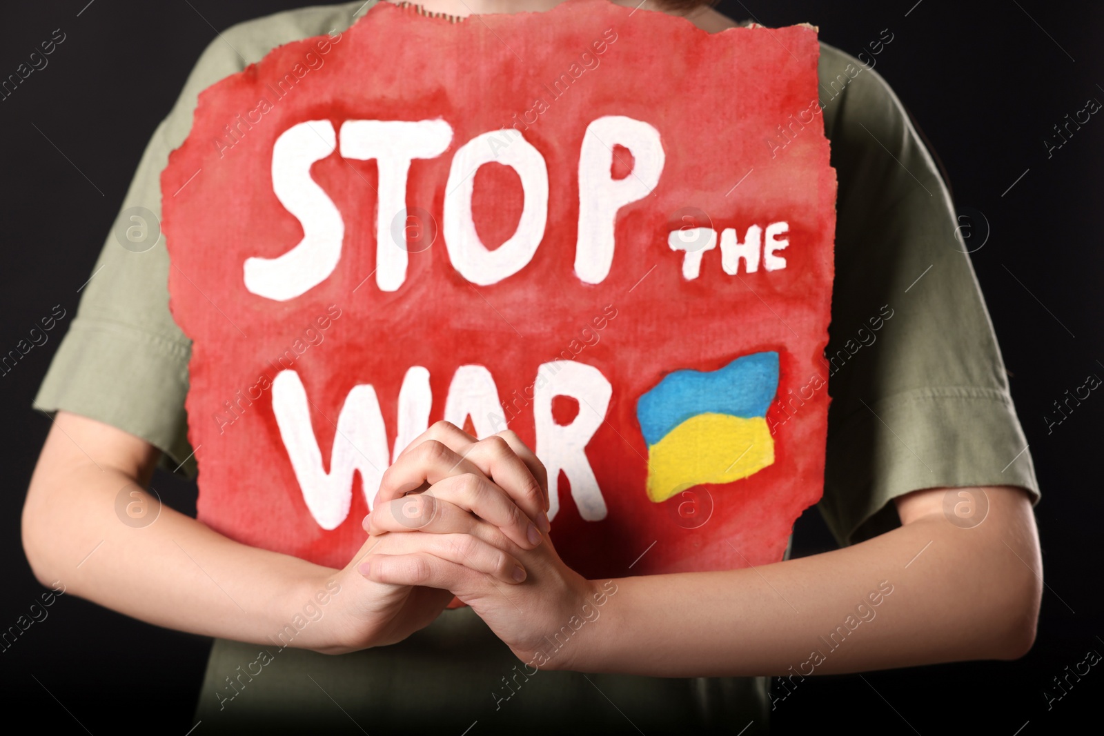 Photo of Woman holding poster with words Stop the War on black background, closeup