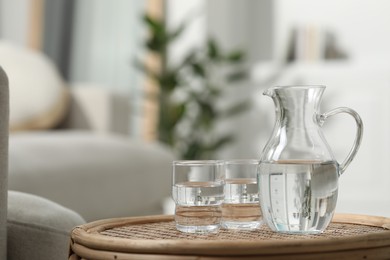 Photo of Jug and glass with water on wicker table against blurred background. Space for text