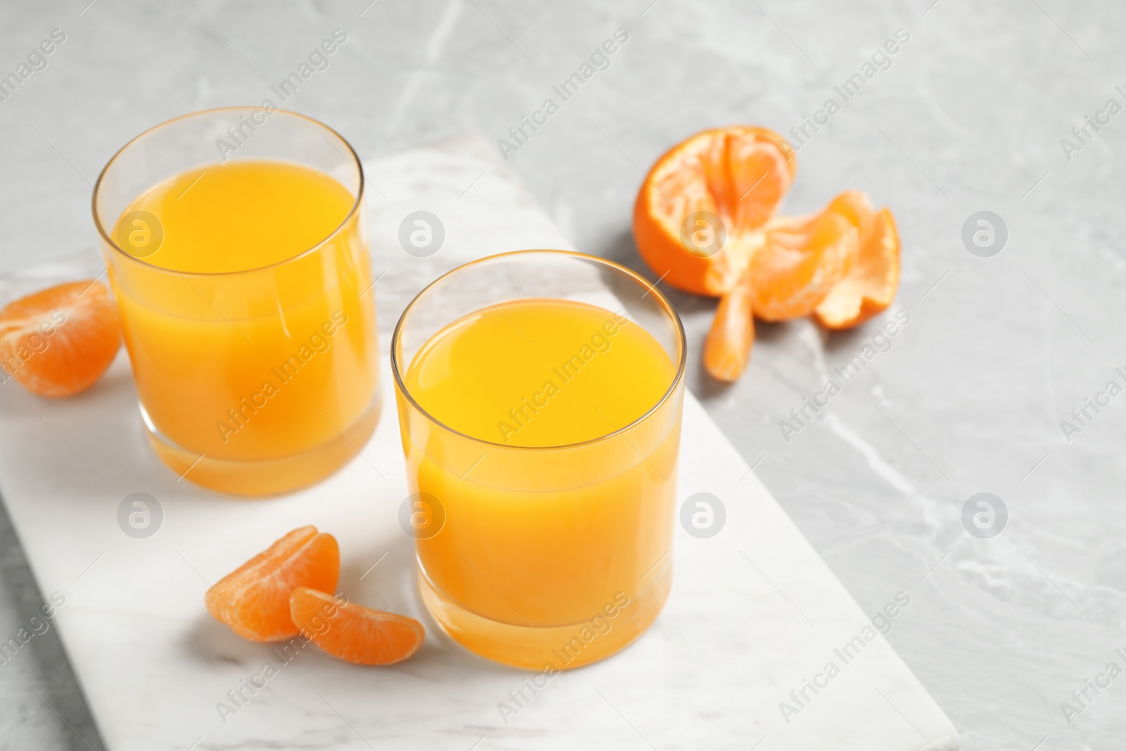 Photo of Glasses of fresh tangerine juice and fruits on light table