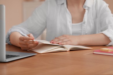 Photo of Woman with notebook at wooden table indoors, closeup