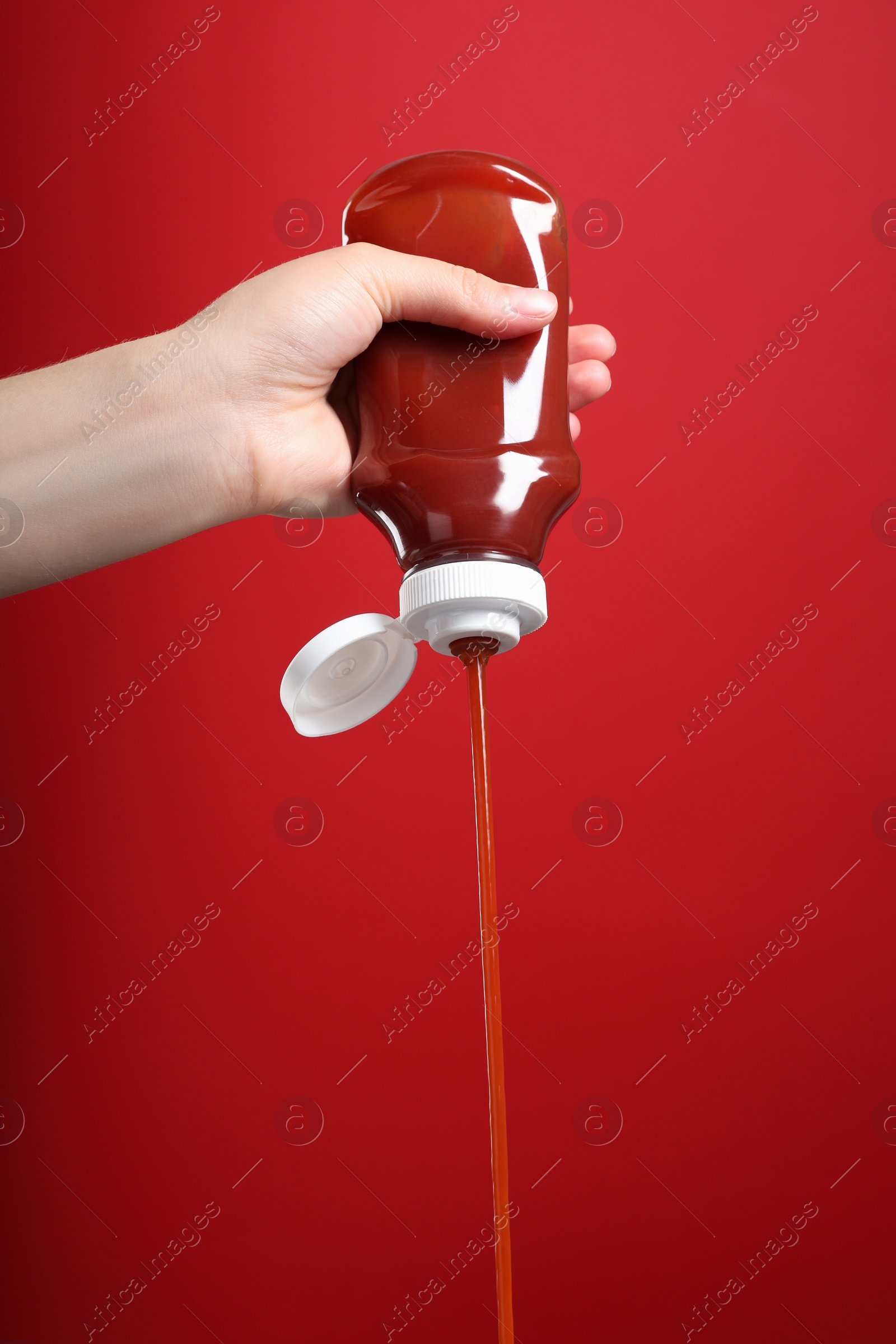 Photo of Woman pouring tasty ketchup from bottle on red background, closeup