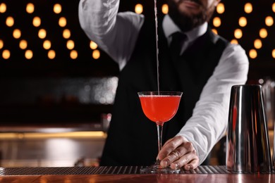 Photo of Bartender preparing fresh Martini cocktail in glass at bar counter, closeup