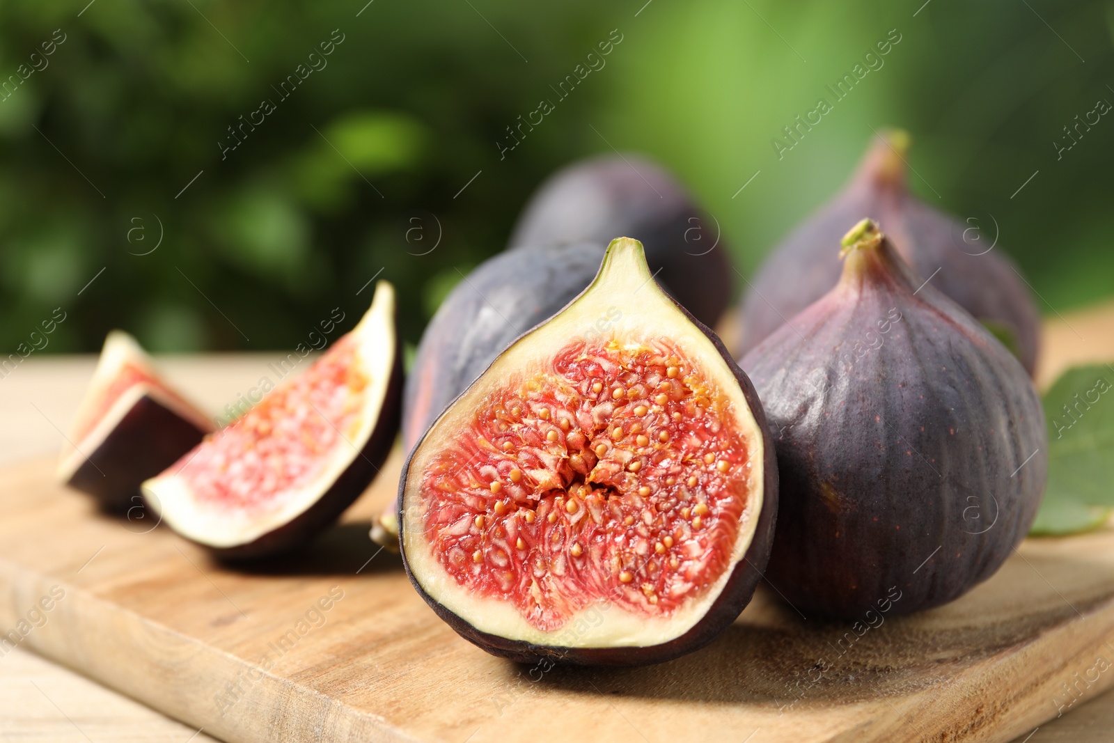 Photo of Whole and cut ripe figs on wooden table against blurred green background, closeup