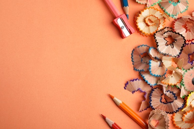 Photo of Color pencils, sharpener and shavings on orange background, flat lay. Space for text