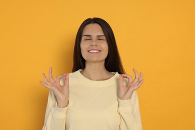 Photo of Young woman meditating on orange background. Zen concept