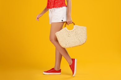 Young woman with stylish straw bag on yellow background, closeup