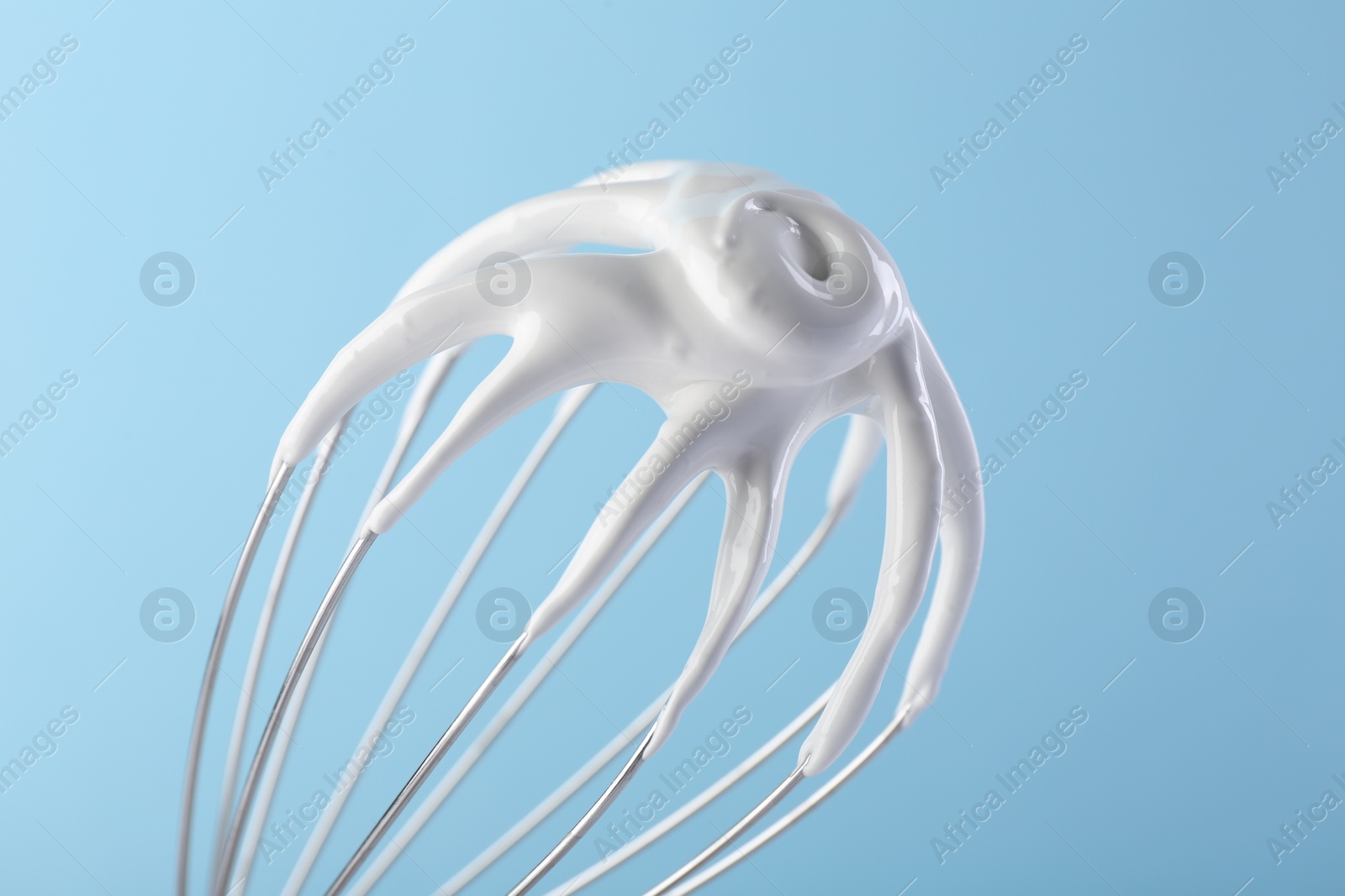 Photo of Whisk with whipped cream on light blue background, closeup