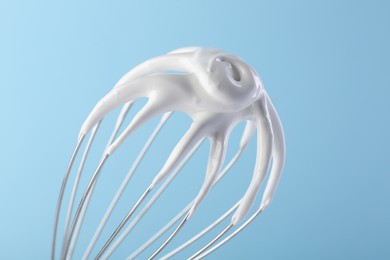 Photo of Whisk with whipped cream on light blue background, closeup
