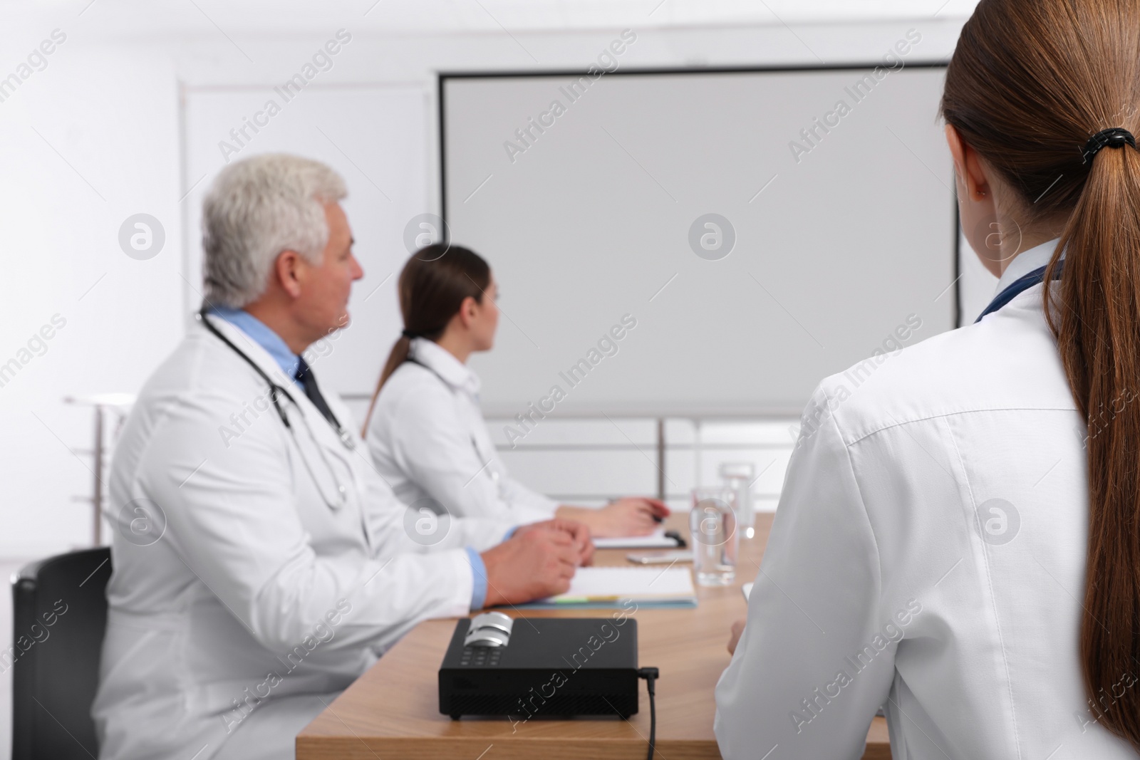 Photo of Team of doctors using video projector during conference indoors