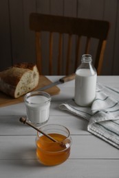 Jar with honey, milk and bread on white wooden table