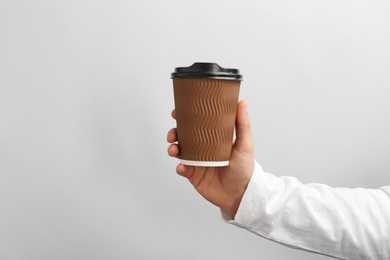 Man holding takeaway paper coffee cup on light background