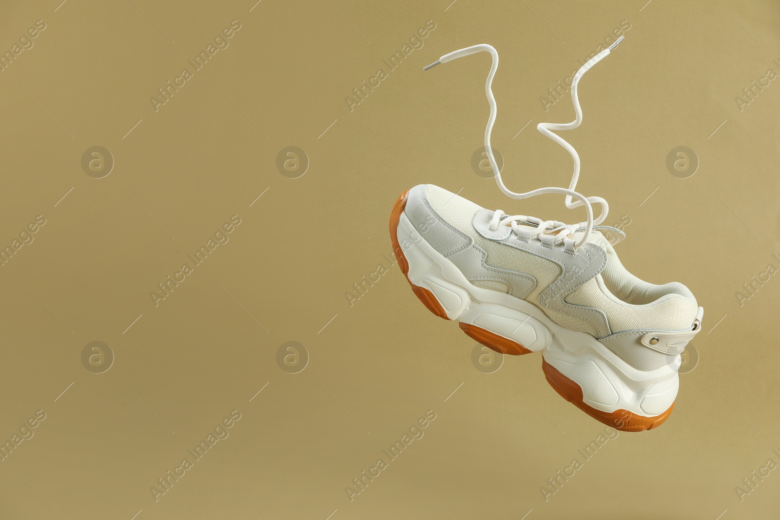 Photo of One new stylish sneaker in air against beige background, space for text