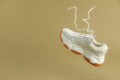 Photo of One new stylish sneaker in air against beige background, space for text