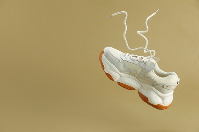 One new stylish sneaker in air against beige background, space for text