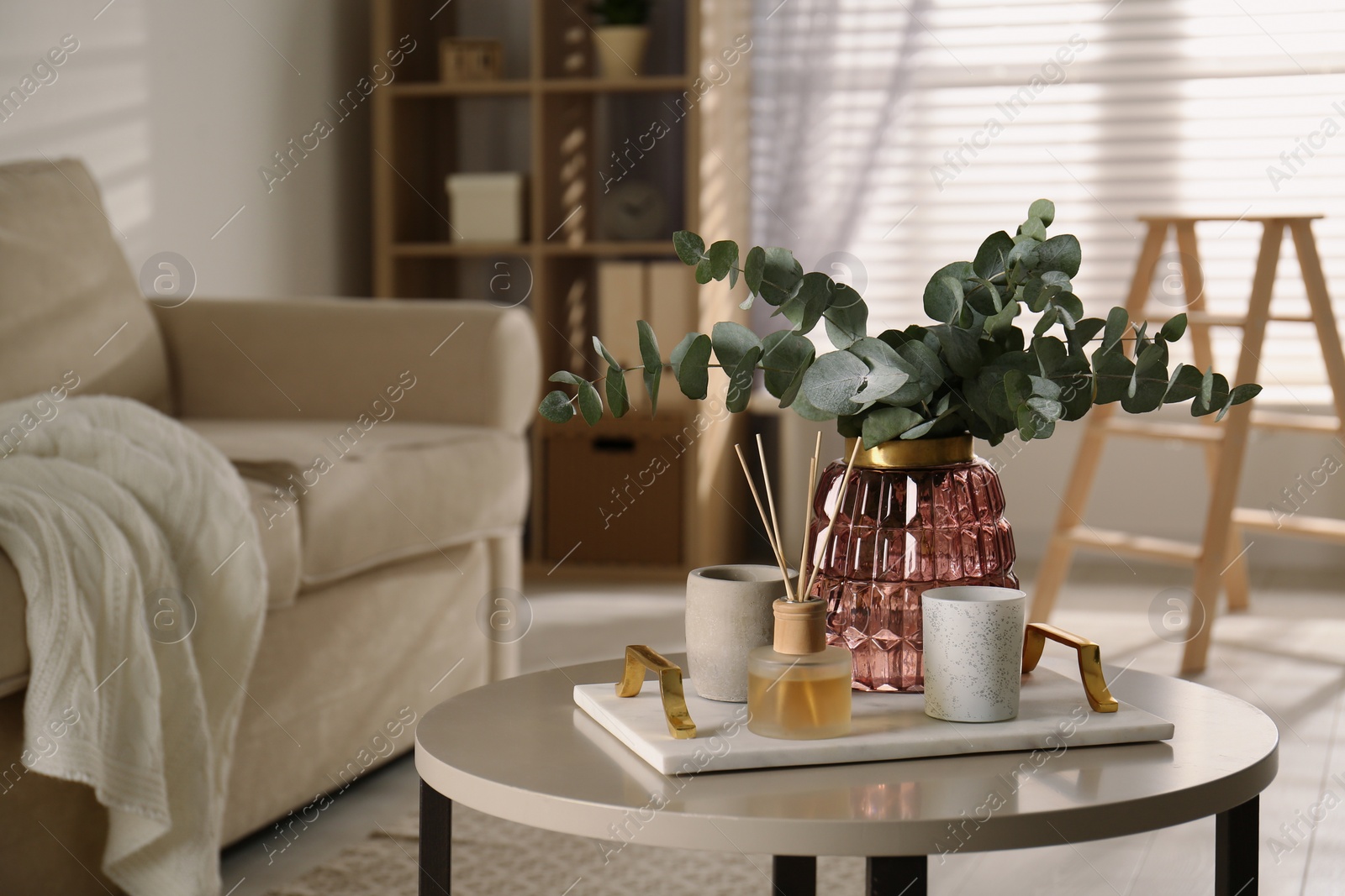 Photo of Bunch of eucalyptus branches and oil diffuser on table in living room. Interior design