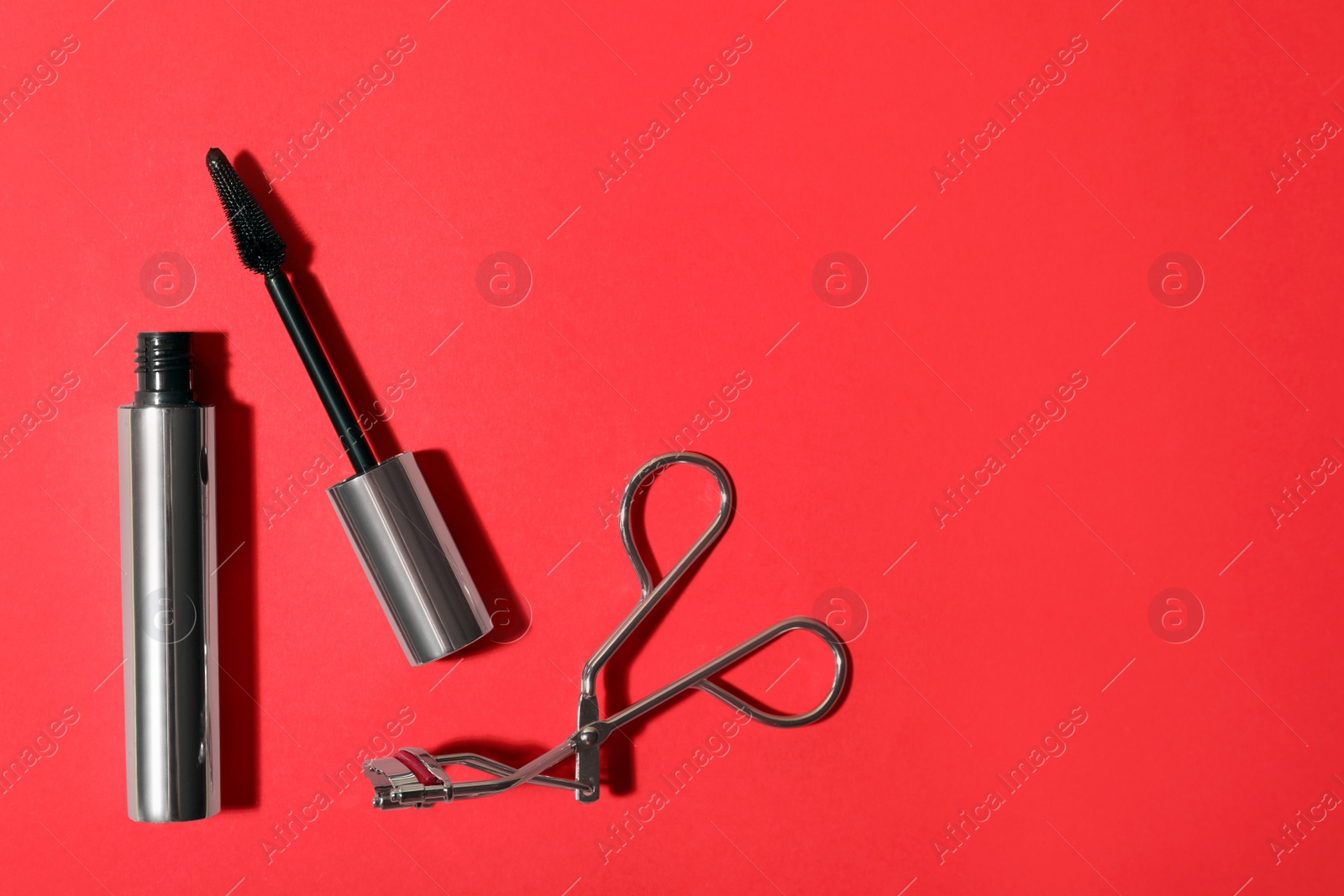 Photo of Black mascara and eyelash curler on red background, flat lay with space for text. Makeup product
