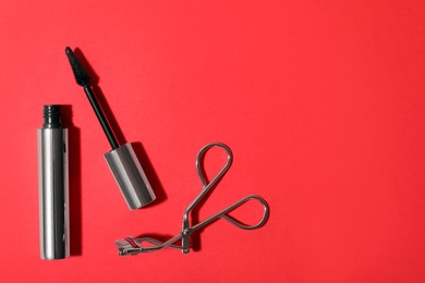 Photo of Black mascara and eyelash curler on red background, flat lay with space for text. Makeup product