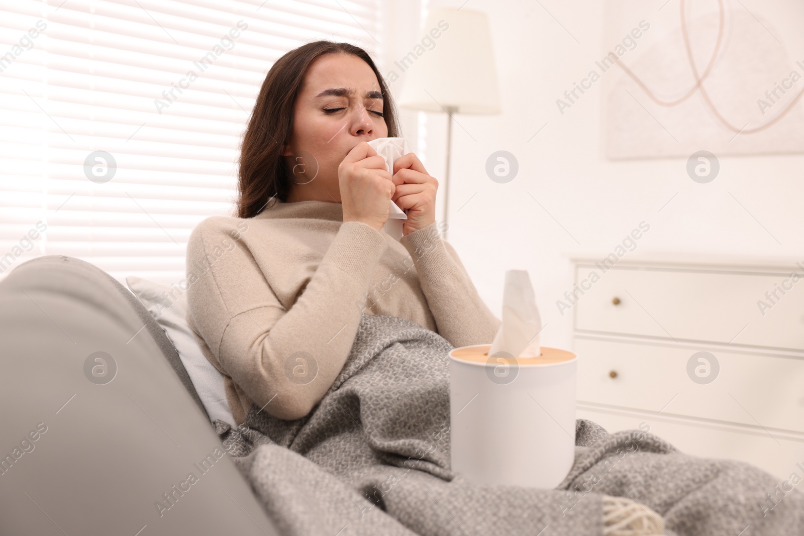 Photo of Sick woman with tissue on sofa at home. Cold symptoms