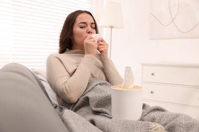 Sick woman with tissue on sofa at home. Cold symptoms